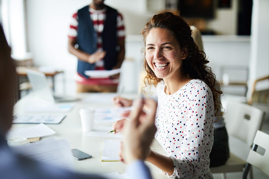 About Our Agency - Happy Businesswoman Sitting at Office Conference Table and Communicating with Her Colleagues During a Meeting